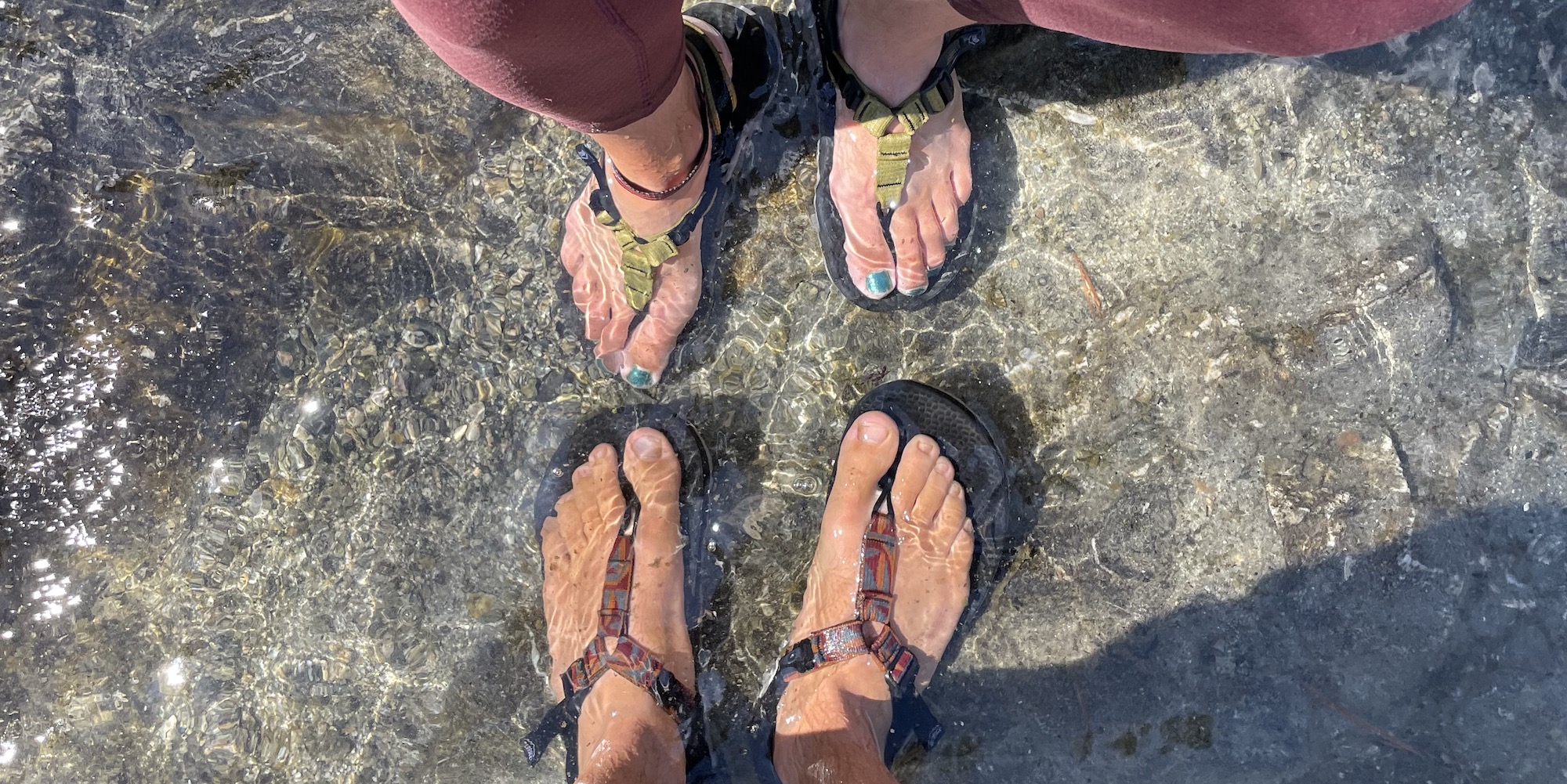 Drop down shot of peoples feet wearing Bedrock sandals in the river