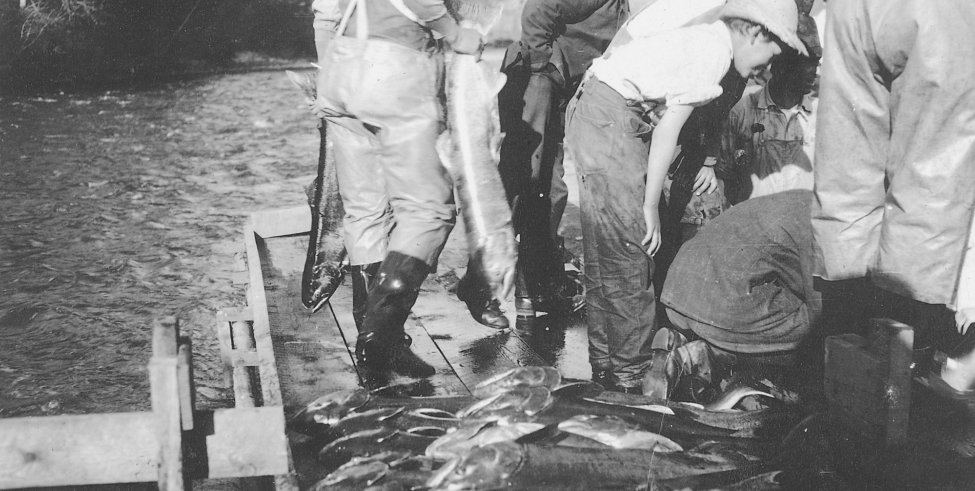 Black and white image of men on a scow boat with a pile of fish they caught on the Salmon River