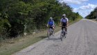 Two bikers moving towards the camera while biking on a paved road in Cuba