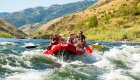 Red raft full of paddlers going through a rapid on the Salmon River Canyons on a sunny and warm day