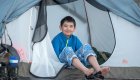 A boy sitting out the zippered door to his tent while camping
